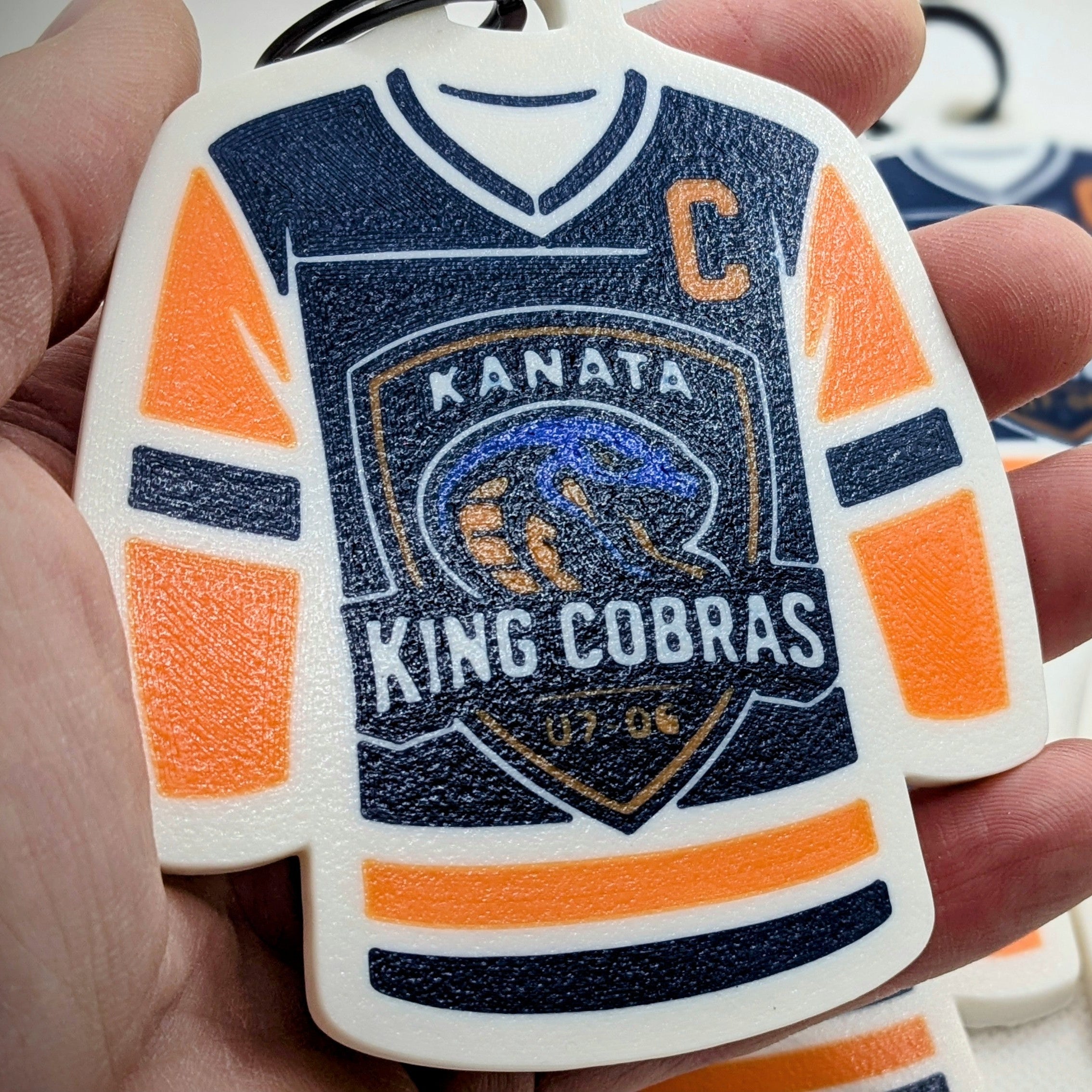 Kanata King Cobras hockey jersey keychain held in a hand with more keychains in the background.